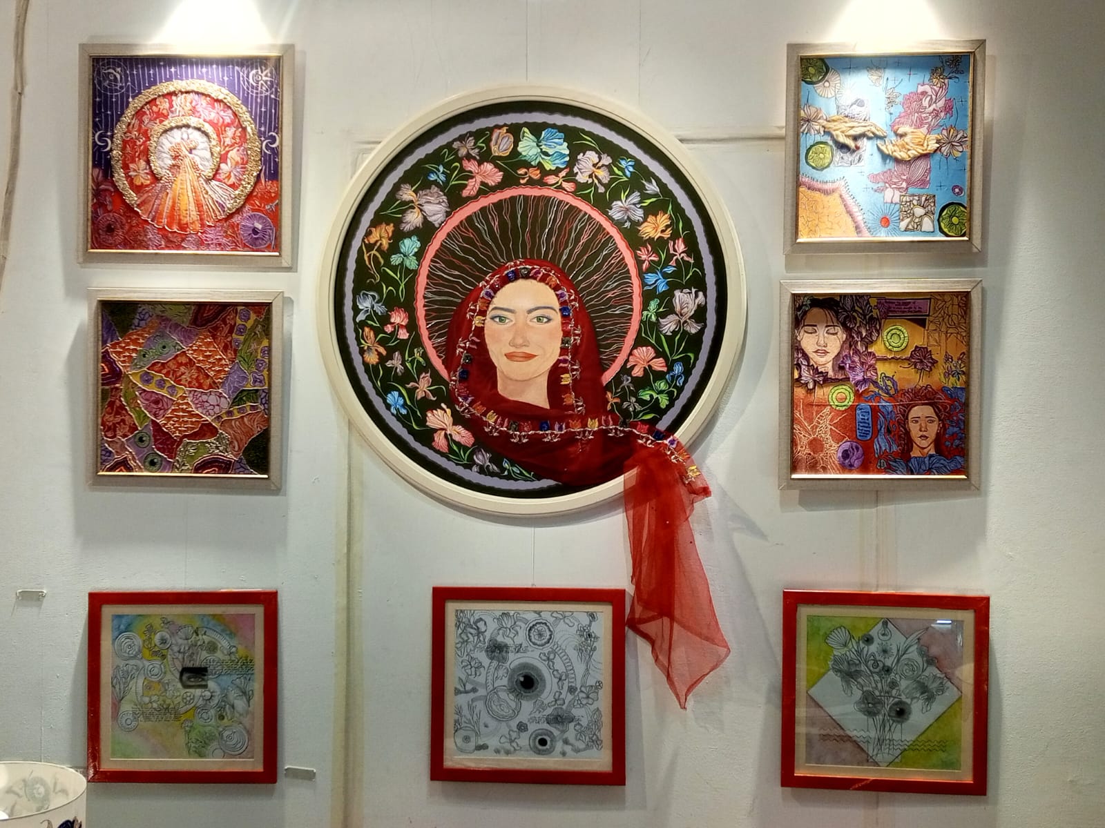 Gallery wall of framed textile works around a large circular portrait with red veil